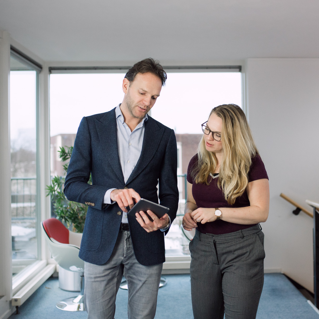 A men holding an i Pad and showing something on it to a women. The men uses his fingers on the i Pad to show something.